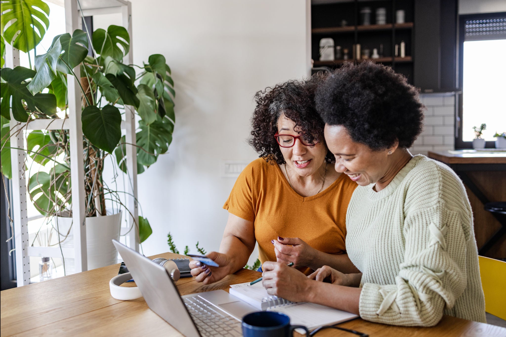 Gay couple sitting at the table in the kitchen and looking at the laptop. They are paying bills and making financial plans.