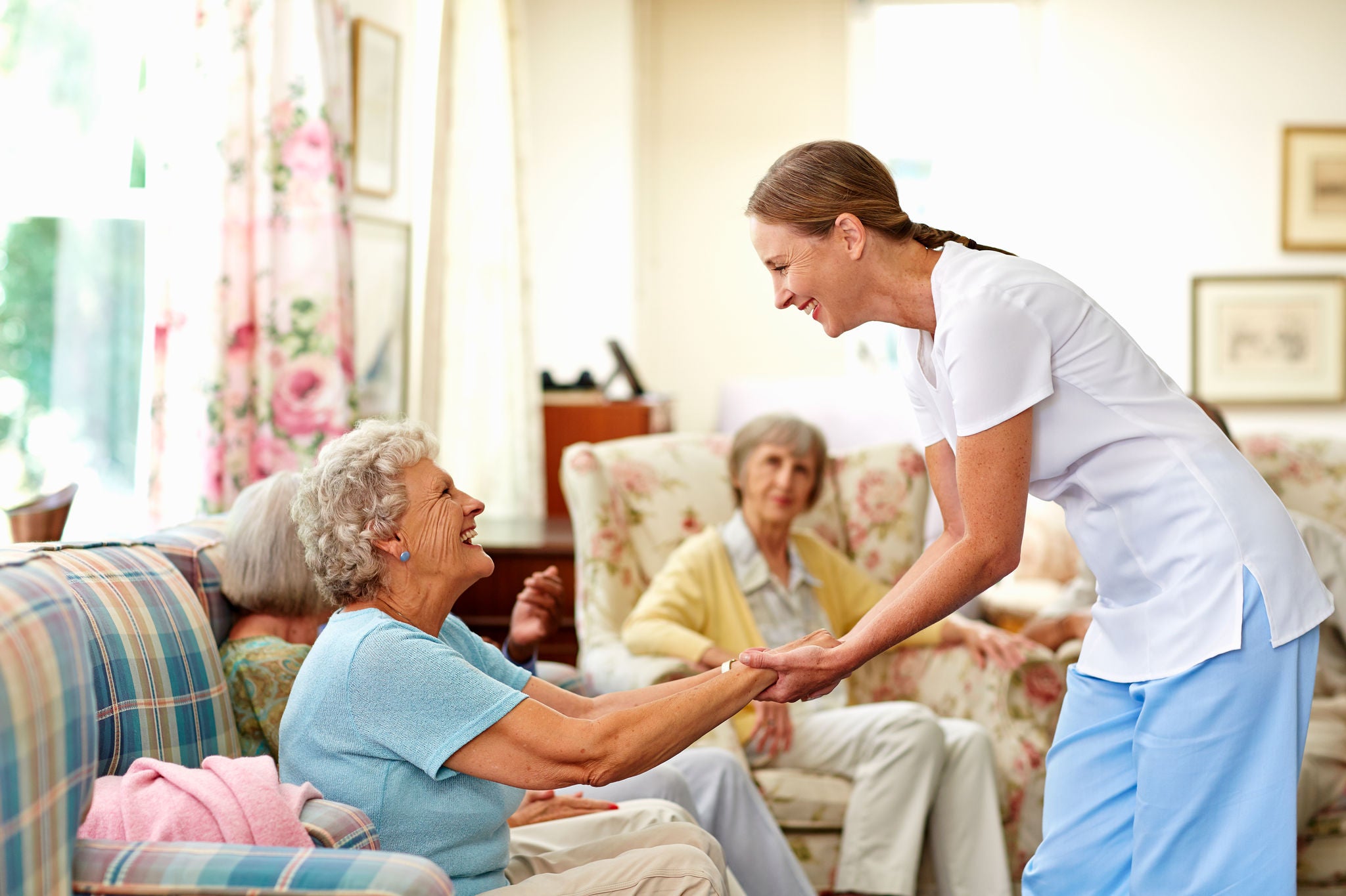 Side view of happy female caretaker assisting senior woman in nursing home