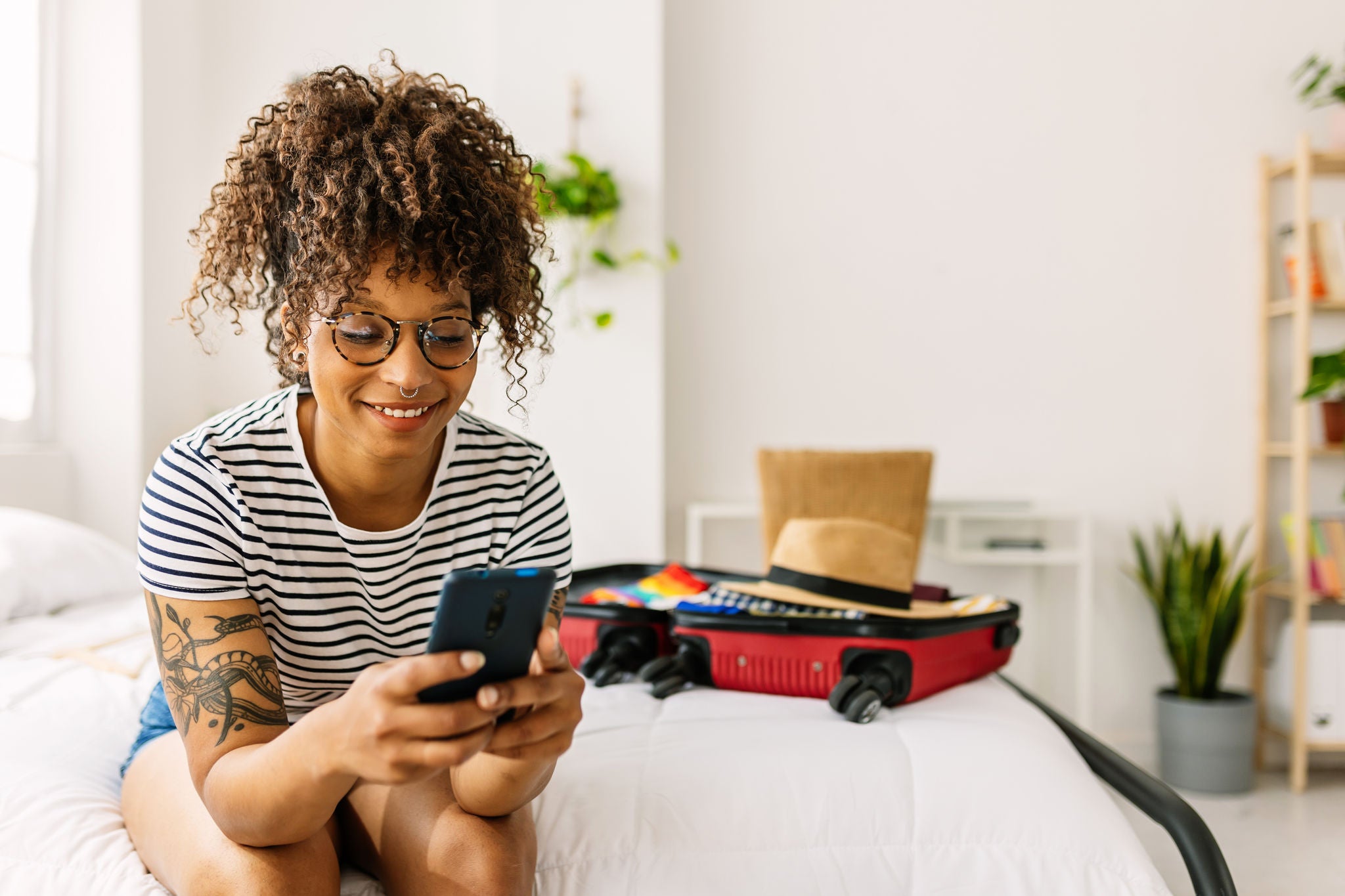 Happy young african american woman booking a hotel room while packing her summer suitcase for holidays