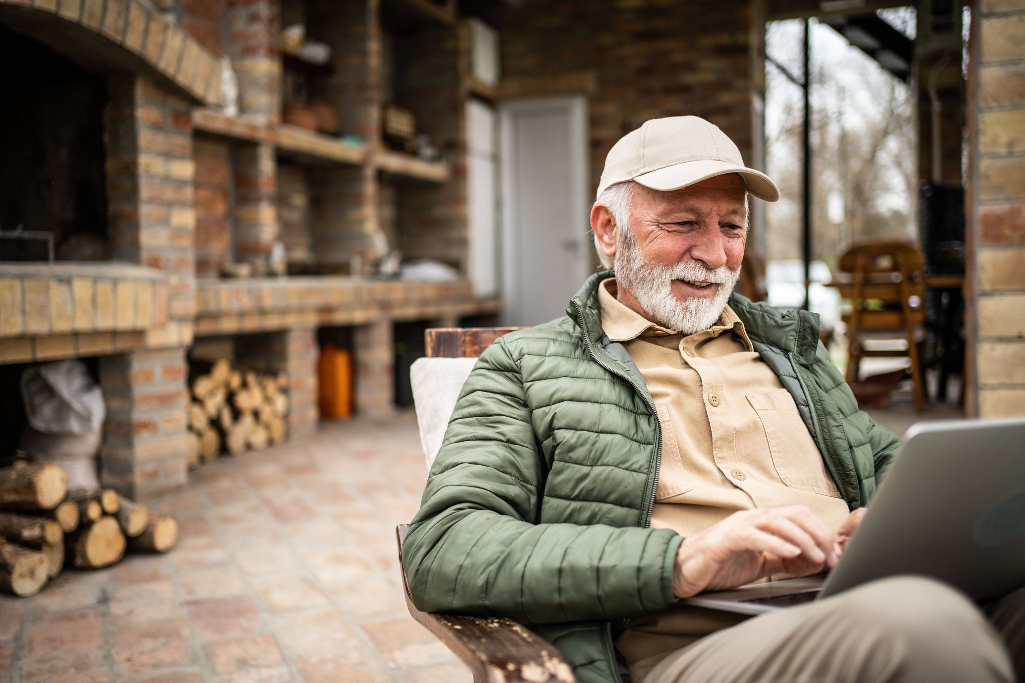 A pensioner sits on the terrace of a cottage and works on a laptop, surfs the Internet or chats online