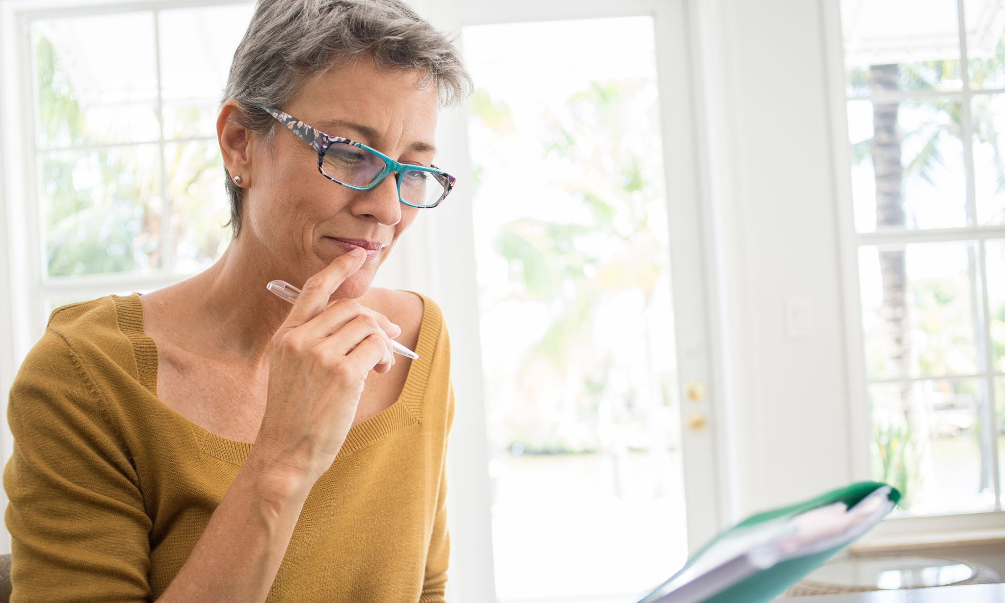 566357241 Woman reading folder at desk in living room