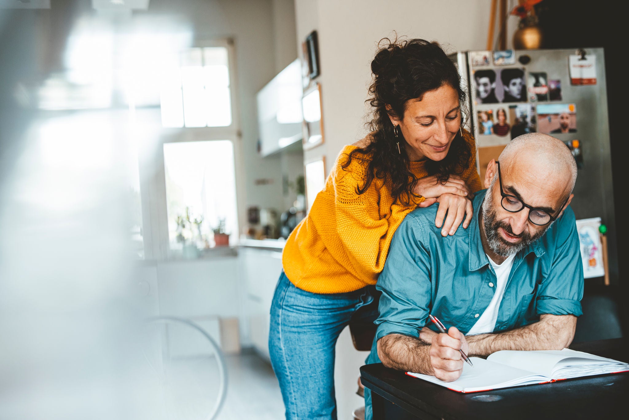 Woman leaning on man writing in notebook at home