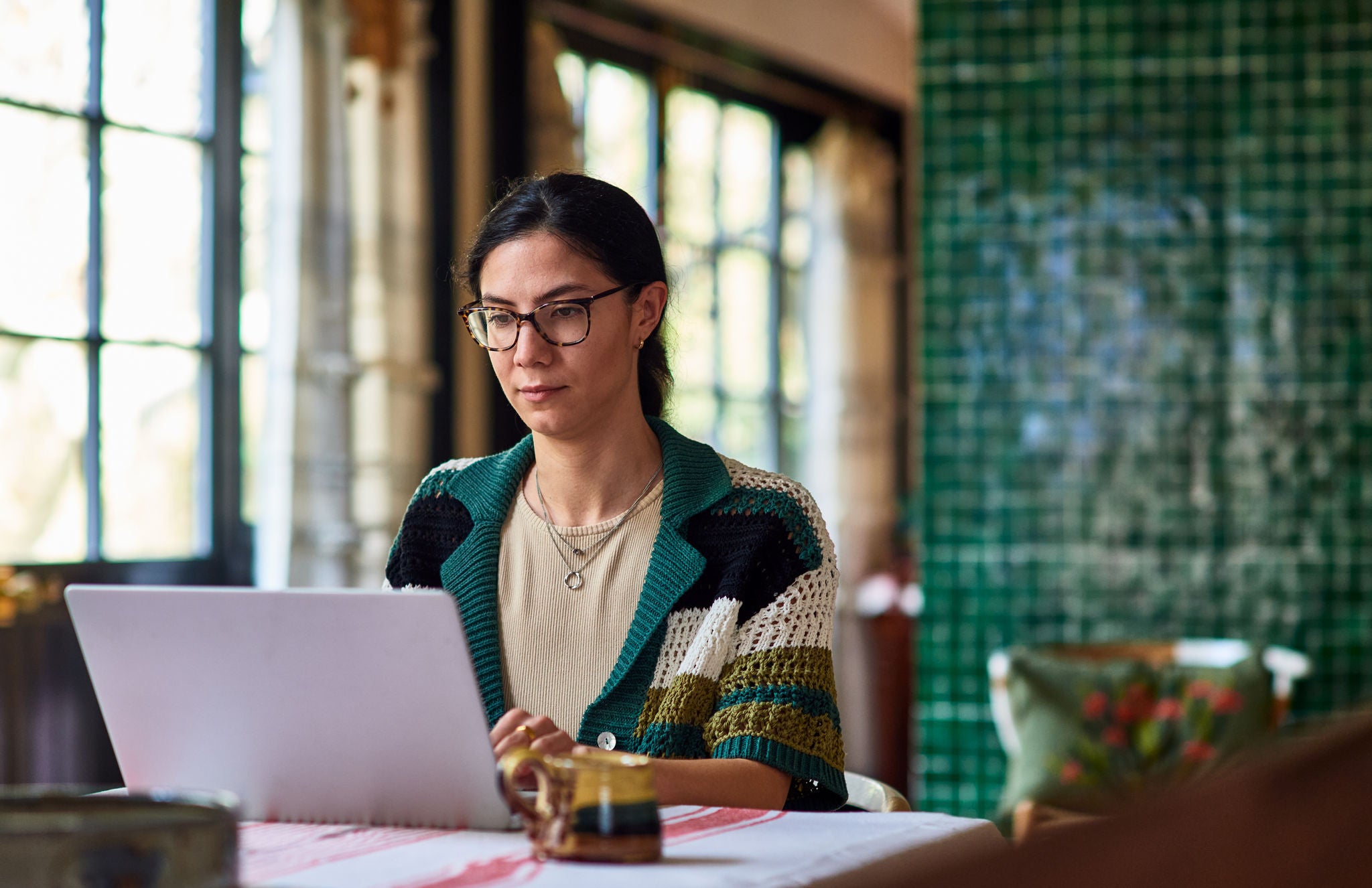 Woman in her 30's working from home sitting at table in dining room using laptop, home office, concentration, connection, working from home