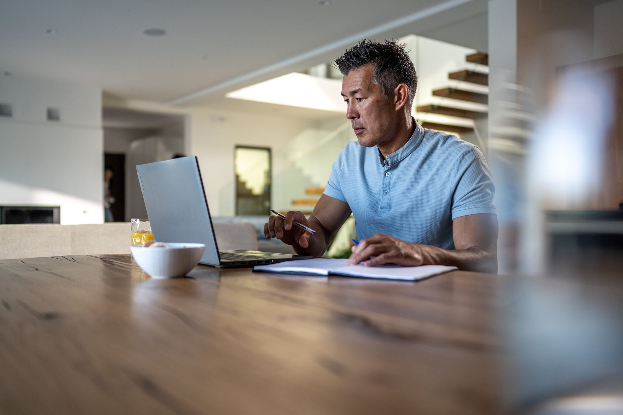 Mature man working on laptop with diary while sitting on chair at home.