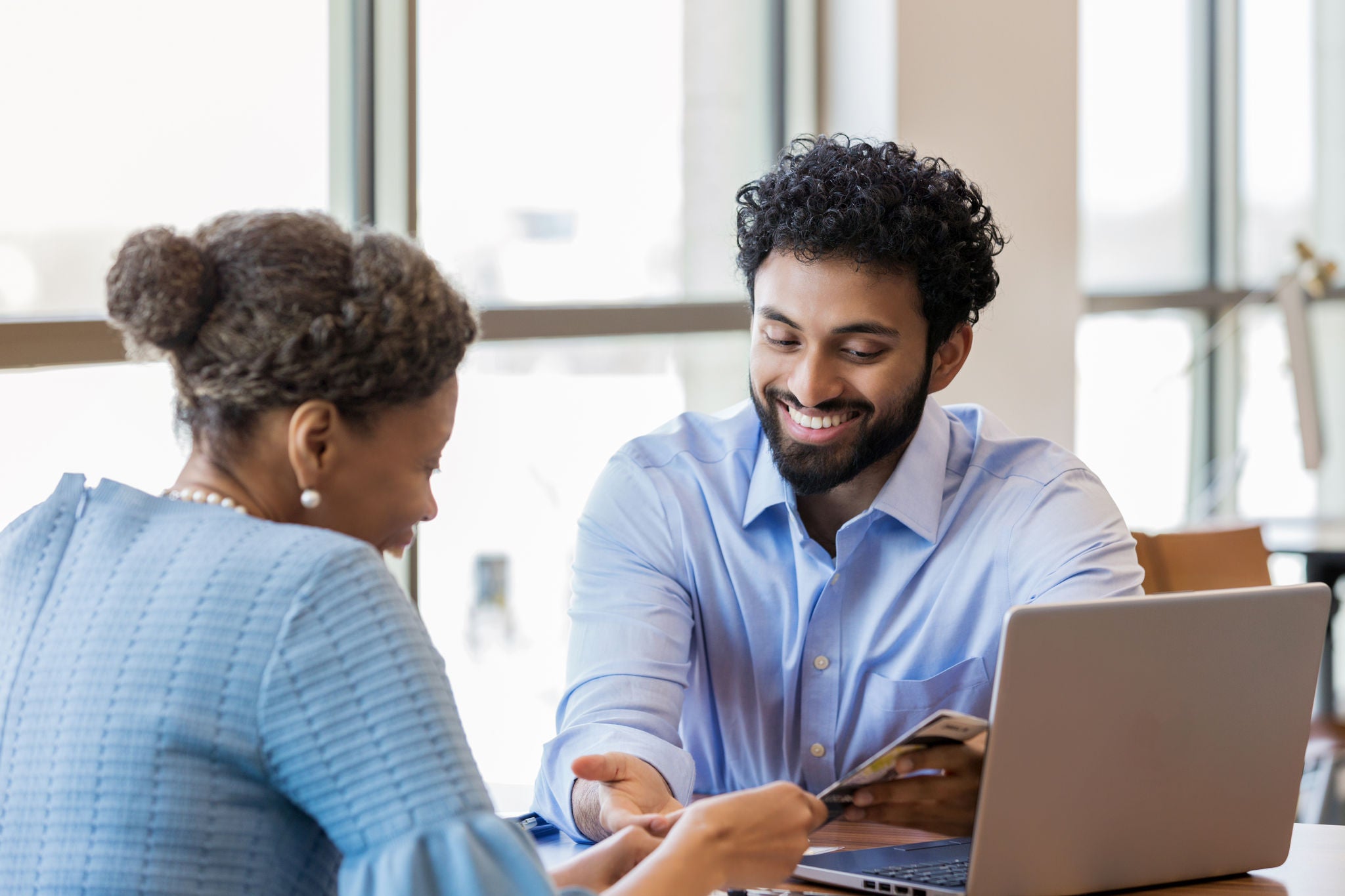 The mid adult account manager of Middle Eastern ethnicity gives an African American woman good news about her retirement account.