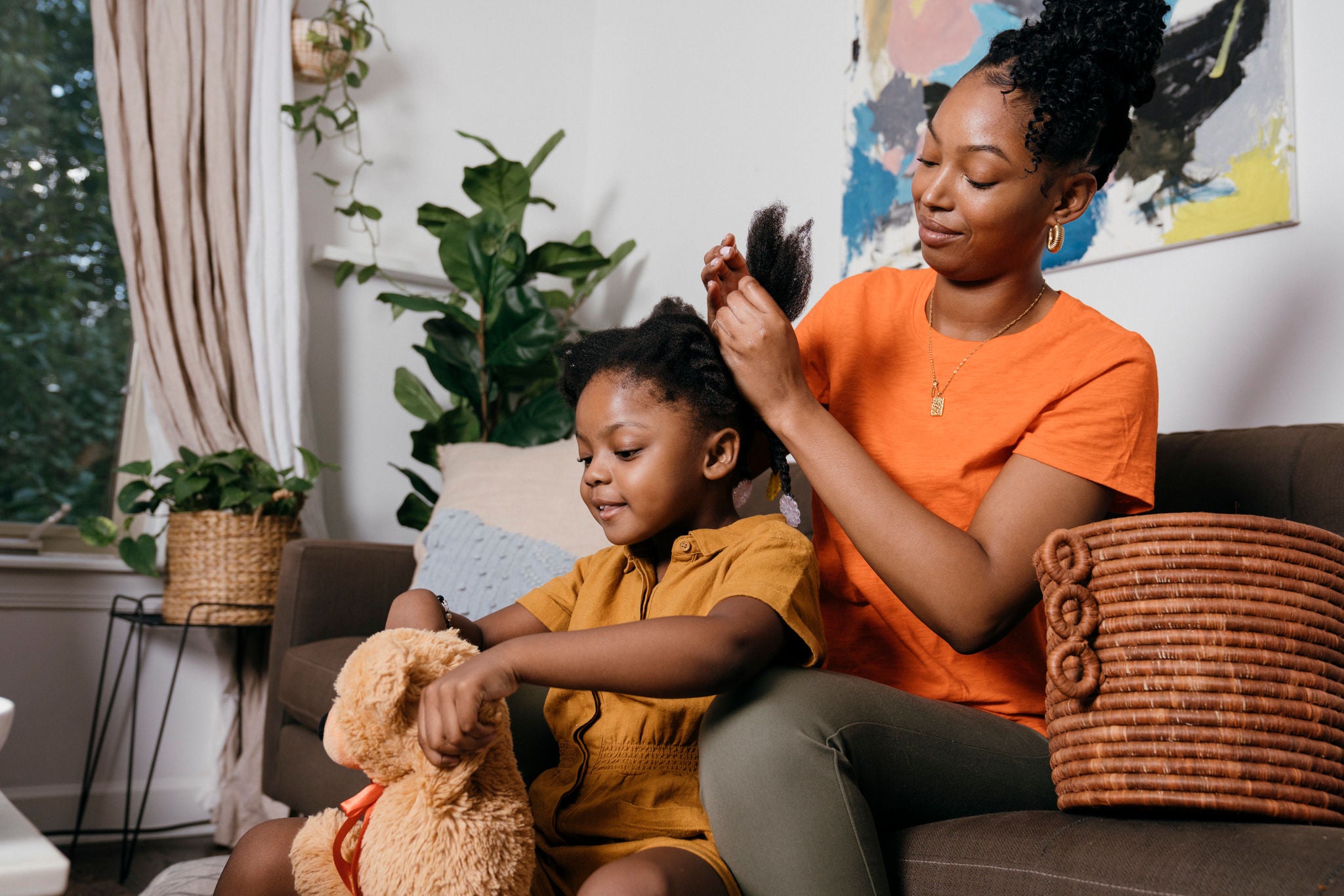 Young  African American female parent braids her daughter's hair at home.