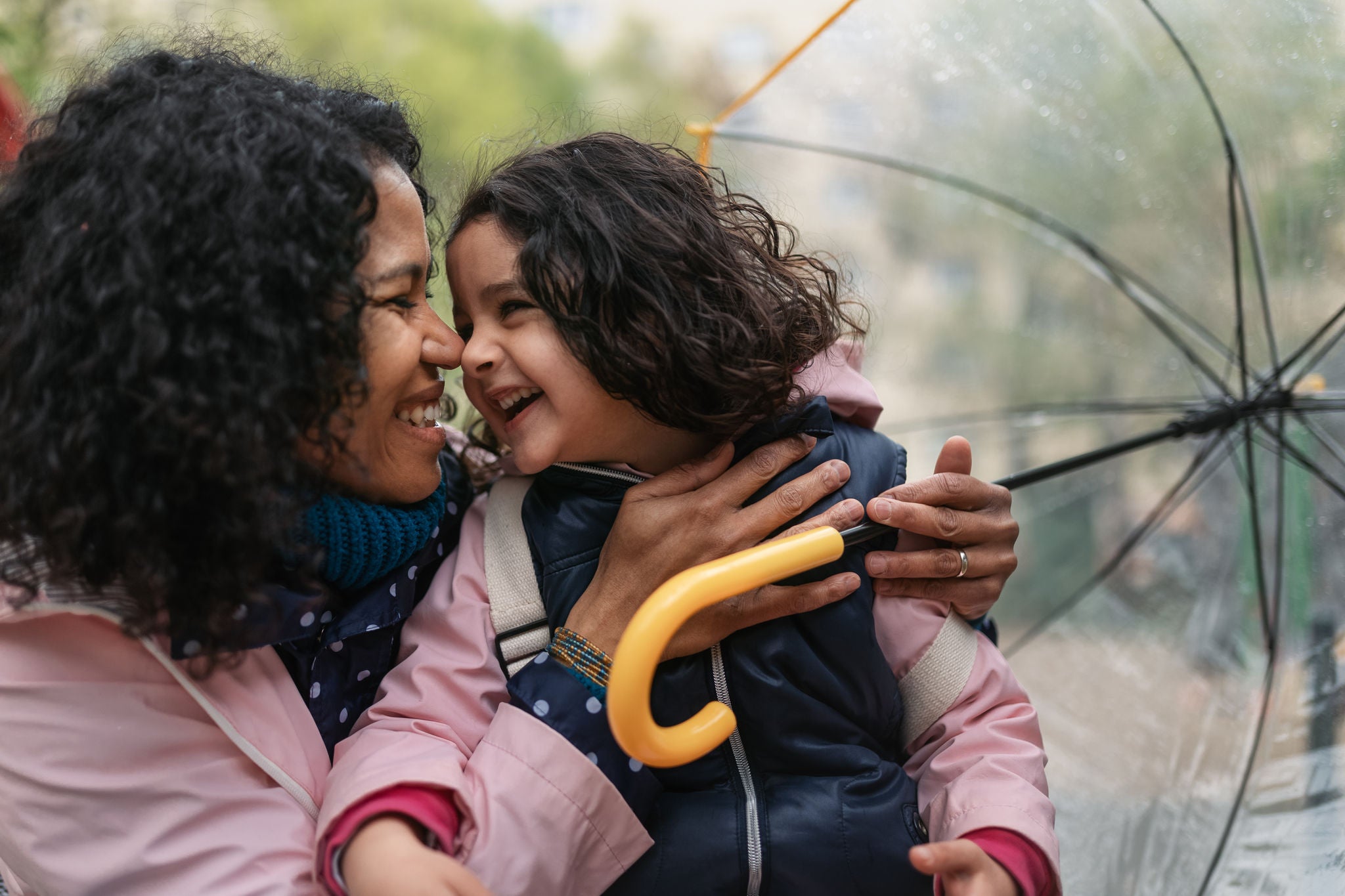 Mother and daughter cuddling outdoor under umbrella.