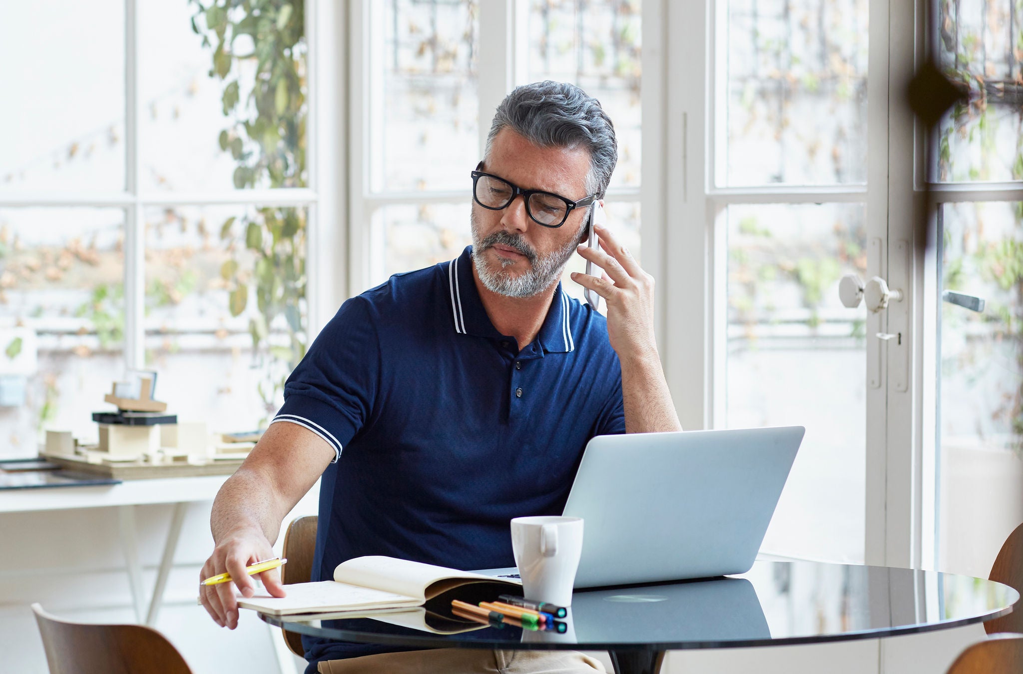 Mature businessman using mobile phone while writing notes at table in office